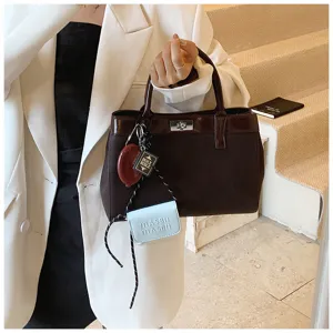 Detailed view of the dark brown handbag with trendy charm pendants and elegant metal lock.