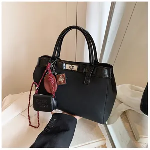 Black fashion handbag detail featuring twist-lock closure, dual top handles, and cute charms.