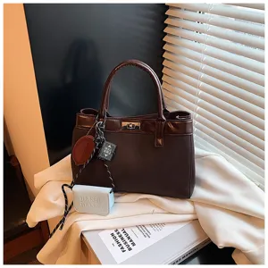 Brown fashion handbag detail view showing exquisite turn-lock closure and cute mini charm.