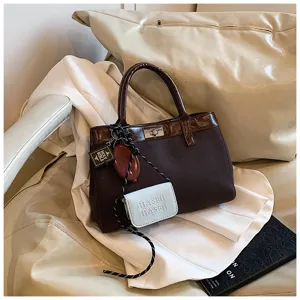 Women's chic brown canvas top handle bag with turn lock closure and stylish charm pendants.