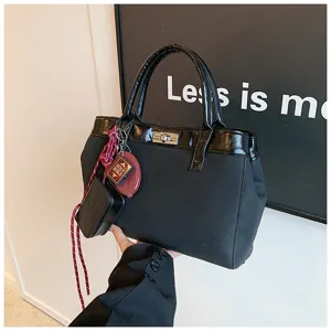 Minimalist black women handbag with patent leather trim, chic charms and top handle.