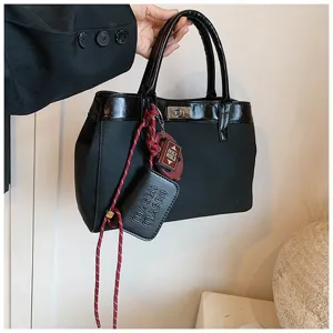 Detailed view of a chic black fashion handbag with contrast glossy trim and decorative lanyard.