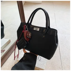 Detailed view of women's black fashion handbag with metal lock, top handles and cute charms.
