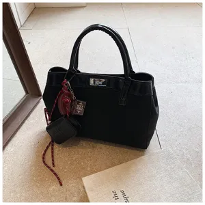 Close-up detail of black canvas tote handbag with chic charms, patent leather trim, and turn-lock.