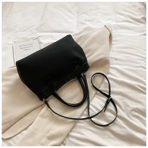 Black minimalist handbag detail lifestyle shot showing leather handles and adjustable shoulder strap.