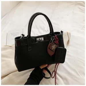 Minimalist black women top-handle crossbody bag with chic turn lock and cute keychain pendant.