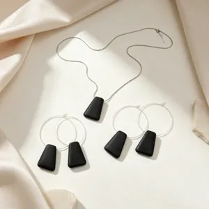 Detailed view of minimalist black geometric pendant necklace and large hoop earrings set.