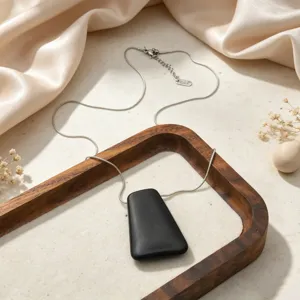 Minimalist geometric pendant necklace detail, sleek metal chain with modern dark charm.