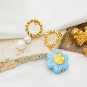 Detailed view of asymmetric gold-plated twisted hoop earrings with pearl and blue glass flower.