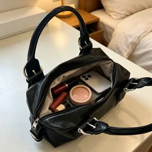 Detail view of black PU leather Boston handbag interior with daily items and metal rings.