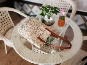 Vista di dettaglio di una borsa in pizzo beige con manici in pelle marrone su un tavolo.