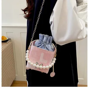 Detail shot of stylish pink bucket bag with denim drawstring and elegant pearl chain handle.
