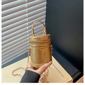Petit sac à bandoulière cylindrique métallique doré avec poignée supérieure et chaîne élégante.