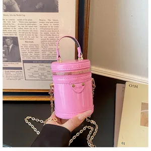 Détail de mini sac bandoulière cylindrique en cuir verni rose, chaîne élégante et poignée.