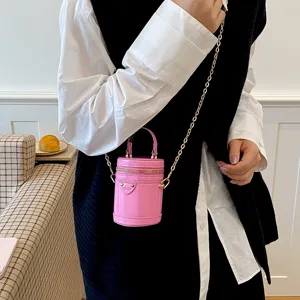Mini sac bandoulière cylindrique rose brillant pour enfants avec chaîne dorée et poignée.