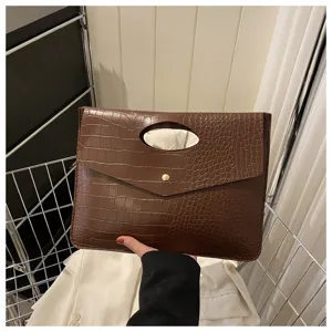 Dettaglio della borsa a clutch marrone con stampa coccodrillo, manico intagliato e bottone.