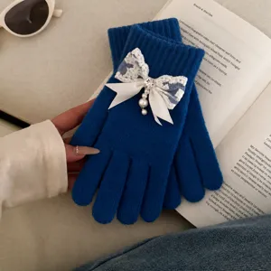 Detail view of blue knit gloves featuring elegant white lace, ribbon bow, pearls, and rhinestones.