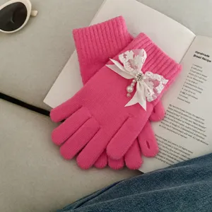 Close-up detail of pink knit gloves featuring elegant lace bow and pearl charms for winter.
