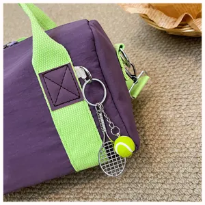Detailansicht der lila zylindrischen Reisetasche mit gründen Riemen und Tennisschlüsselanhänger.