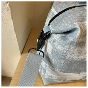 Close up detail view of travel duffel bag strap hook and zipper closure in light blue fabric.
