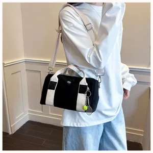 Kleine schwarze Canvas Reisetasche mit weißen Trägern und Tennisanhänger für unterwegs.