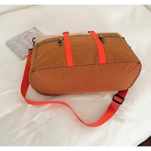 Detail of the grid pattern travel bag with bright orange straps and side zipper pocket.