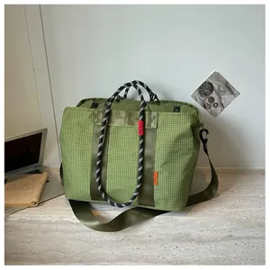 Vue détaillée du sac de voyage à carreaux verts avec poignées et bandoulière fitness.