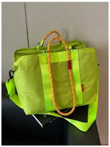 Gros plan détaillé du sac de voyage quadrillé vert fluo doté de poignées en corde orange.