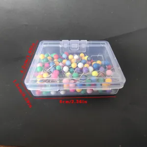 Chinchetas de colores en una caja de almacenamiento de plastico transparente vista de frente.