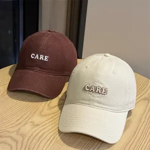 Detail view of casual cotton baseball caps in maroon and beige with CARE embroidery.