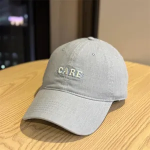 Detailed view of the casual light grey baseball cap featuring cute embroidered CARE text design.