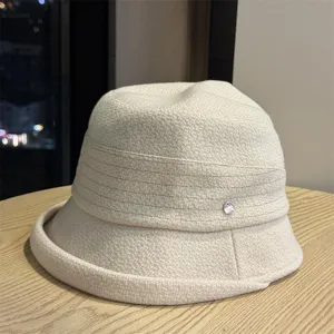 Detail view of a beige knitted bucket hat featuring a textured fold and silver accent.