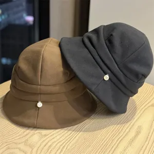 Close-up detail of autumn pleated bucket hats in black and brown colors with chic metal charms.
