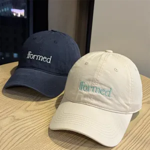 Detailed view of embroidered letter baseball caps in navy and beige, cotton fabric.