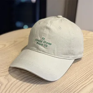 Nahaufnahme der beige baseballkappe mit grüne bestickte schriftzügen auf der krone.