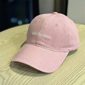 Pink washed baseball cap detailed view, showing front embroidered text and textured cotton fabric.