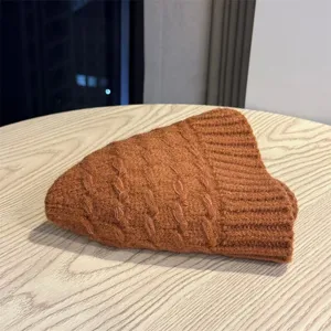 Detail shot of brown cable-knit winter beanie hat folded neatly on a wooden table surface.