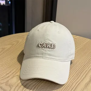 Detail shot of the beige baseball cap showing front CARE letter embroidery and fine stitches.