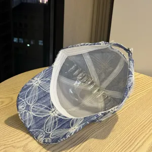 Detailansicht der gewaschenen Jeans-Baseballkappe mit weißer Blumenstickerei und Innenschutz.