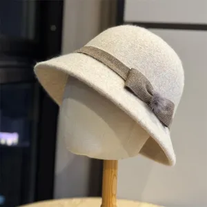 Close-up detail of the beige felt bucket hat with brown ribbon and pom-pom decor.