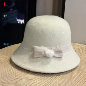 Detail shot of the elegant beige wool felt bucket hat with a bow and fur ball accent.