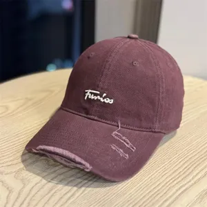 Close-up of distressed maroon baseball cap with white cursive embroidery, soft crown design.