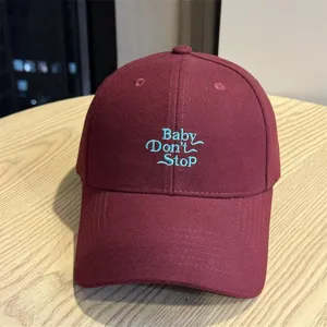 Close-up detail shot of maroon baseball cap featuring blue embroidered text design.