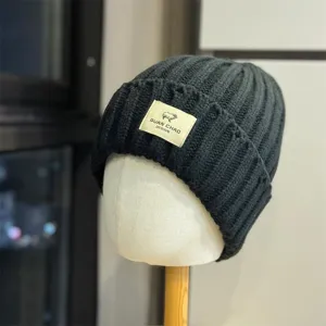 Detailed view of dark grey knitted winter beanie with sheep logo patch, soft wool warm hat.