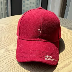 Détail casquette de baseball en laine rouge, visière courbée avec broderie et style.