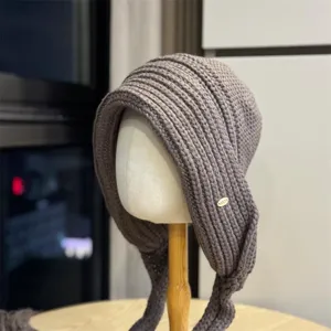 Detailansicht der graubraunen Strickmütze mit Ohrenklappen, weiche Textur und kleines Schild.