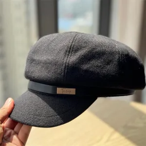 Detailed view of the dark grey wool newsboy cap featuring a chic leather strap and metal badge.