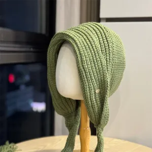 Detailansicht einer kuscheligen grünen Strickmütze mit Ohrenklappen und Metall-Logo.