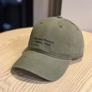 Close-up detail of the army green embroidered baseball cap, showing fine front lettering and stitch.
