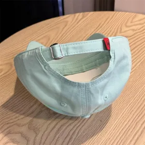 Detail view showing the adjustable metal buckle and red tag of the light green soft baseball cap.
